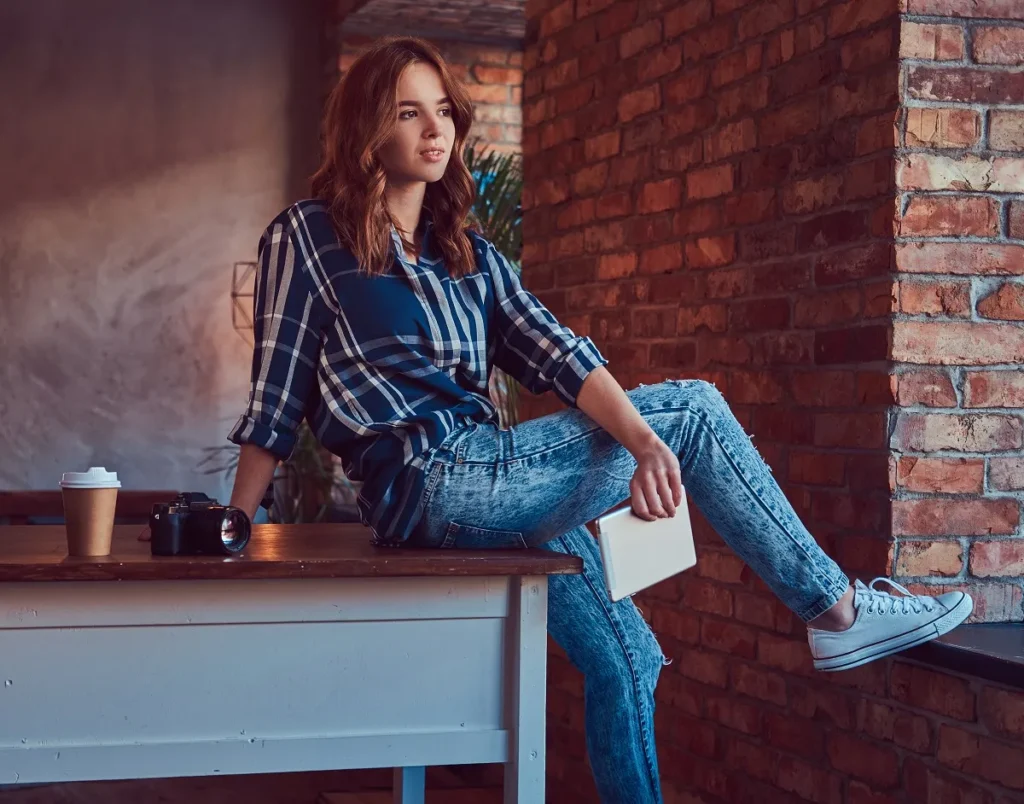 young charming girl photographer working with tablet sits table studio with loft interior