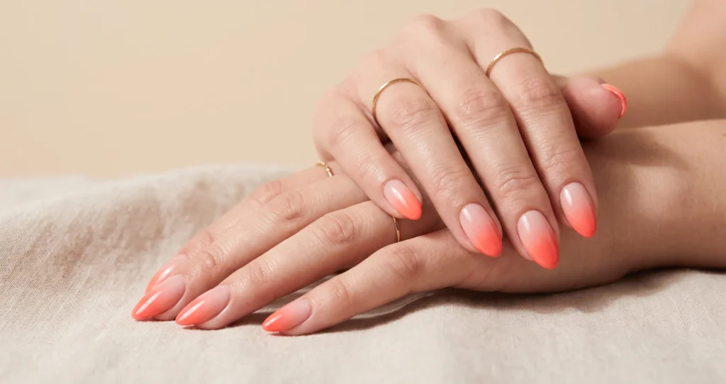 Gradient ombre coral nails softly blending from nude-pink into vivid coral.