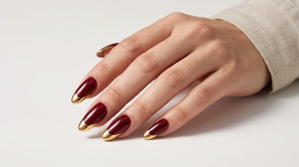 Burgundy and Gold Nails: 10 Luxurious Ideas, Shades & Pro Tips for a Rich Manicure 10 High-shine burgundy and gold nails with mirror-finish reflective gold chrome tips in bright daylight.