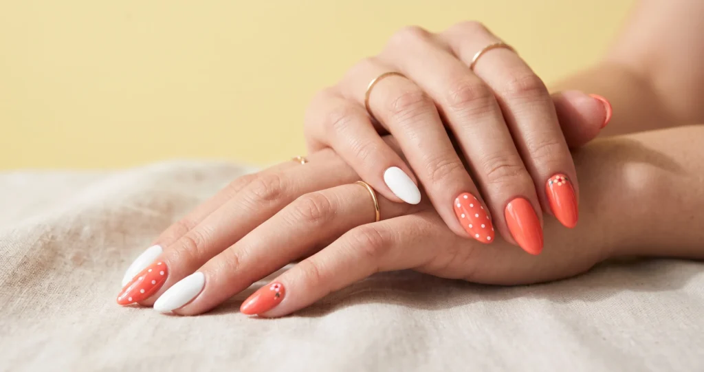 Playful coral nails paired with fresh white nail art accents on a bright background.