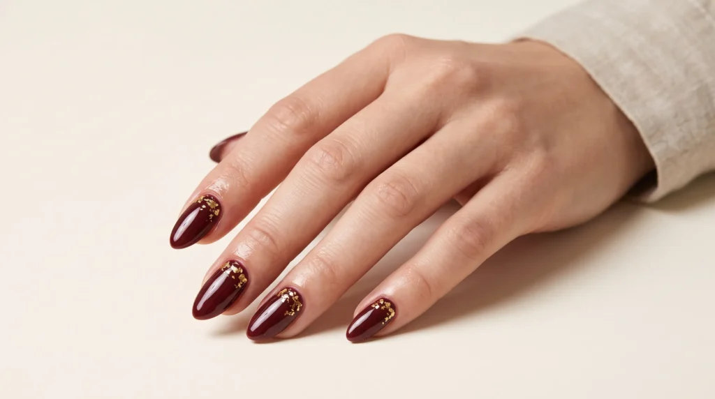 Burgundy and Gold Nails: 10 Luxurious Ideas, Shades & Pro Tips for a Rich Manicure 4 Rich burgundy and gold nails detailed with organic metallic gold foil flakes under bright lighting.